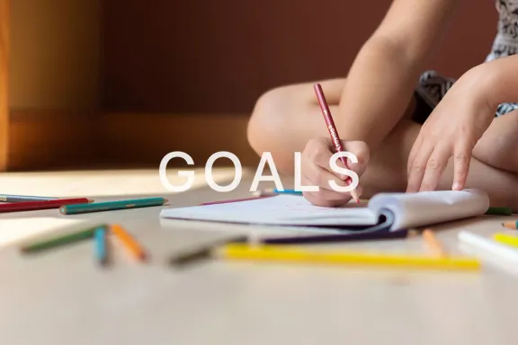 Student writing in a notebook with the word Goals across the image